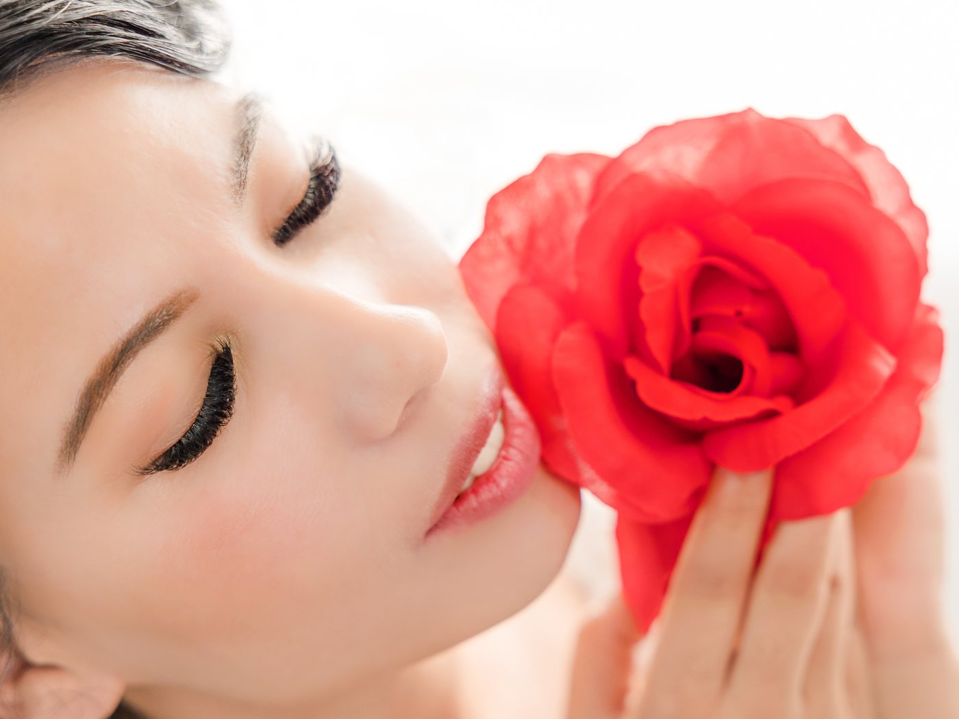 Volume lash extensions, eyes closed, holding a red rose